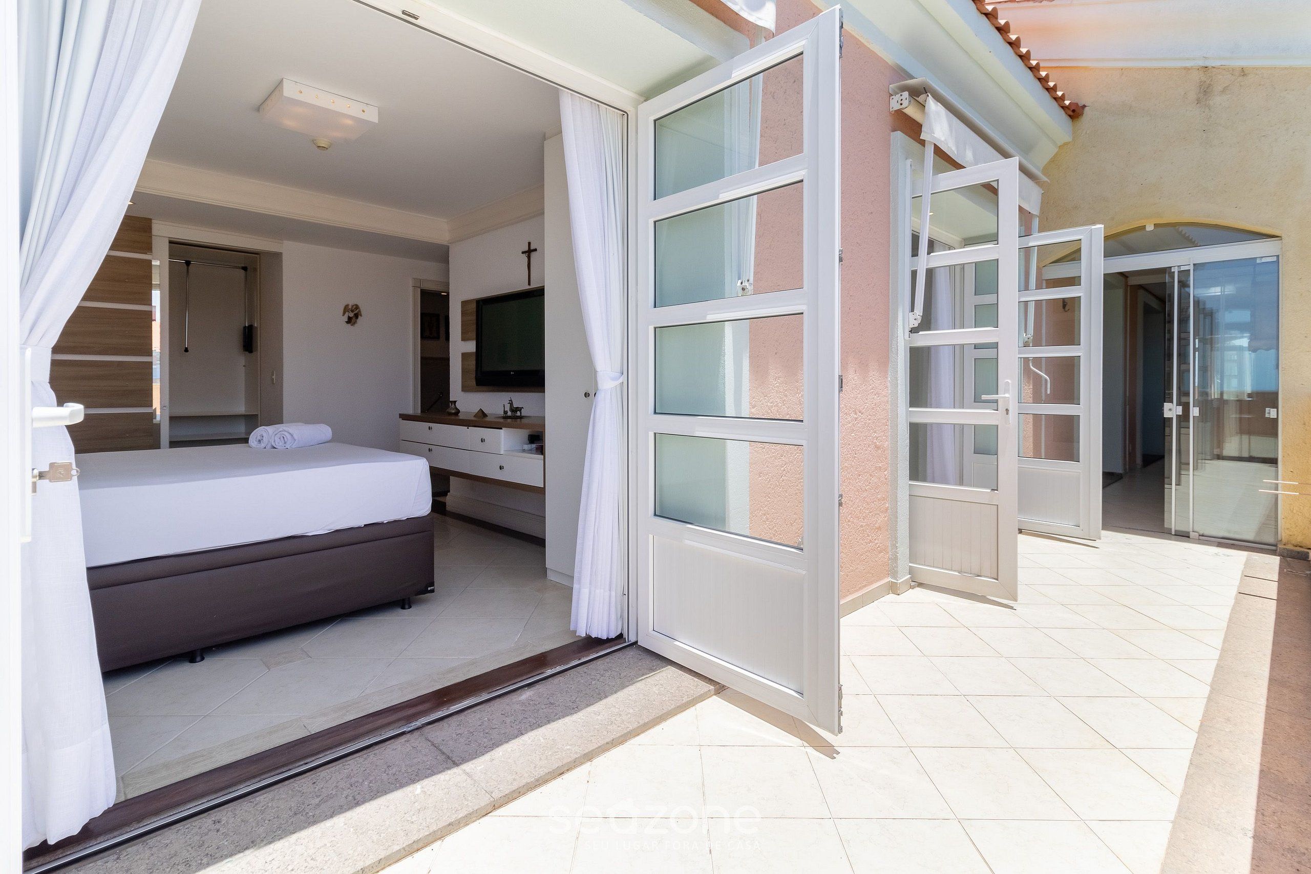 Ein Hotelzimmer mit Bett, Fernseher, Badezimmer und einer Glasschiebetür, die auf einen Balkon führt.