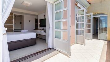 A hotel room with a bed, a TV, a bathroom, and a sliding glass door leading to a balcony.