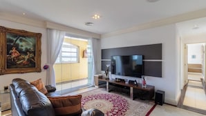Ein modernes Wohnzimmer mit einem großen Flachbildfernseher, einem Ledersofa, einem gemusterten Teppich und einem Gemälde an der Wand.