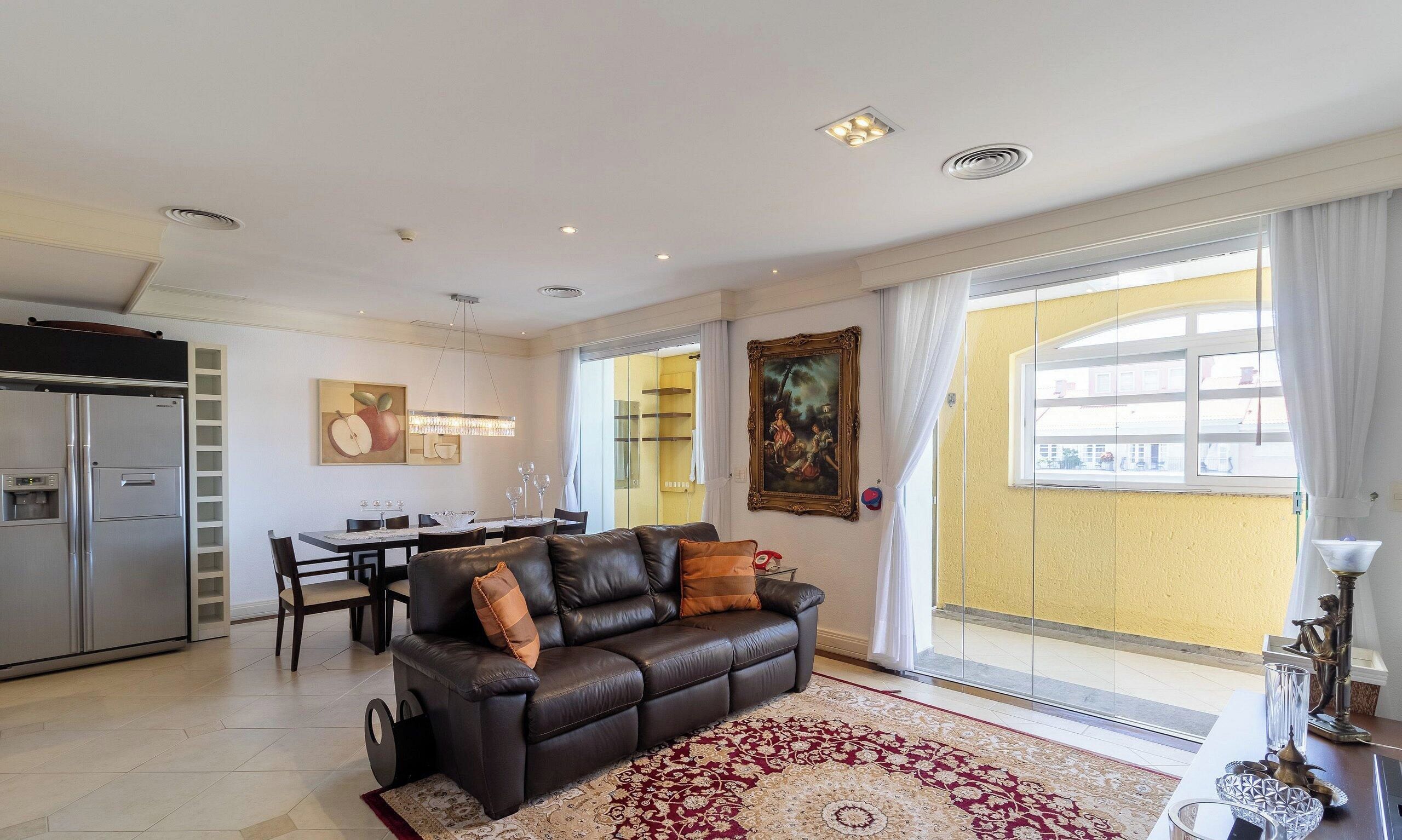 Een moderne woonkamer met een leren bank, een eethoek en een groot raam met gordijnen.