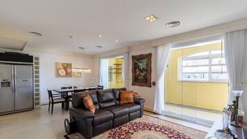 A modern living room with a leather sofa, dining area, and a large window with curtains.