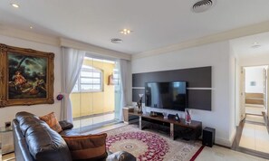 Een moderne woonkamer met een grote flatscreen televisie, een leren bank, een kamerkleed en een schilderij aan de muur.