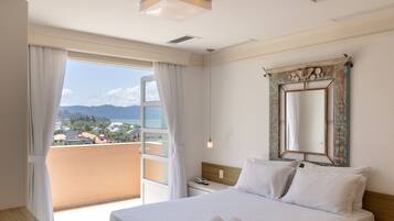 A hotel room with a bed, a bedside table with a phone, a large mirror, and a view of a coastal area.