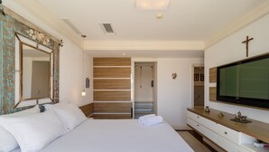 Ein Hotelzimmer mit einem großen Bett, einem Holzschrank, einem Fernseher und einem Kreuz an der Wand.