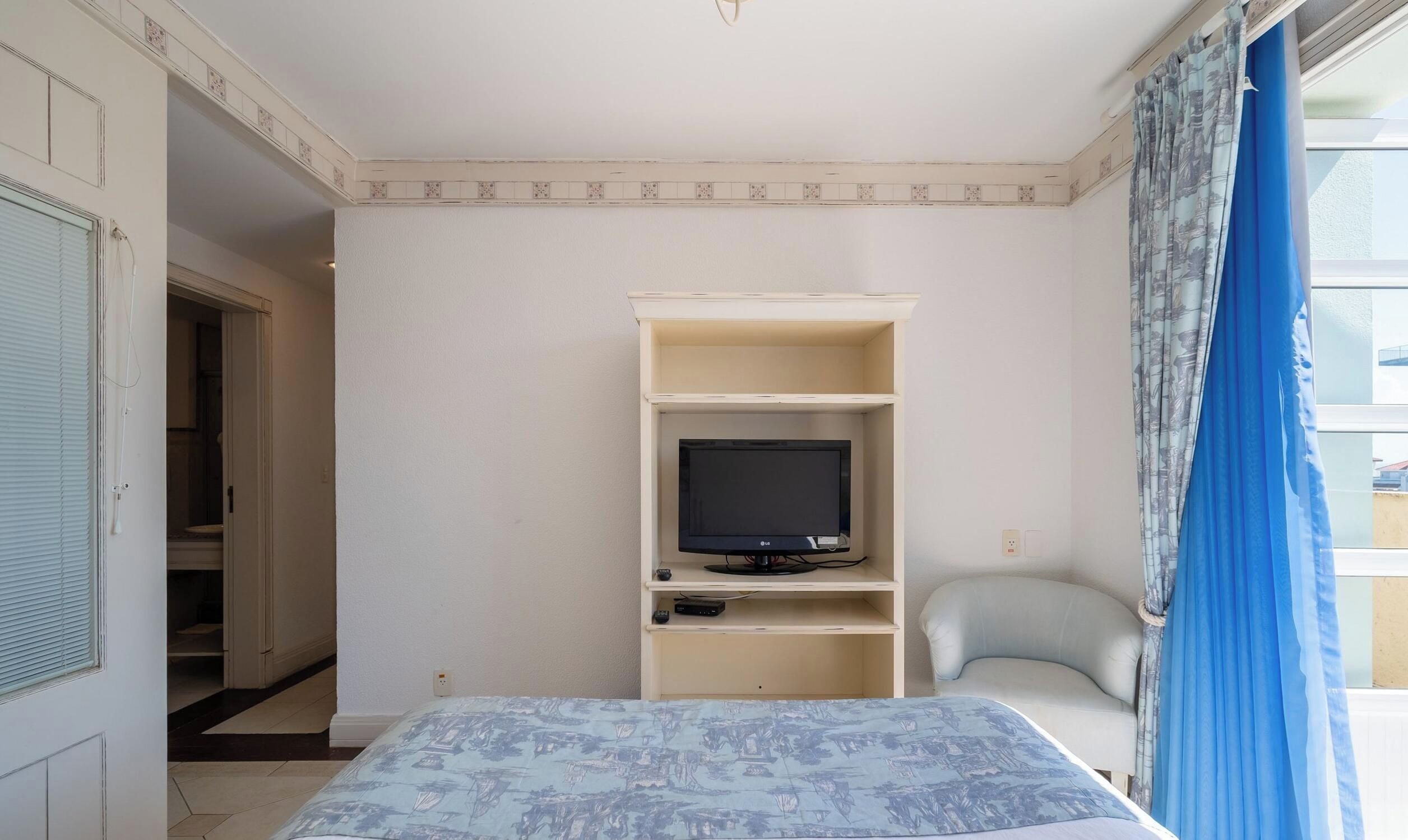 Ein Zimmer mit einem Bett, einem Fernseher auf einem Tisch, einem Sessel und einem Fenster mit Vorhängen.