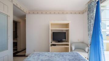 A room with a bed, a television on a stand, a chair, and a window with curtains.