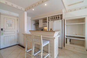 A kitchen with white cabinetry, a microwave, a refrigerator, and a chair. - Exclusive Penthouse Luxury Resort Jurere Ilc2508 (Florianópolis)