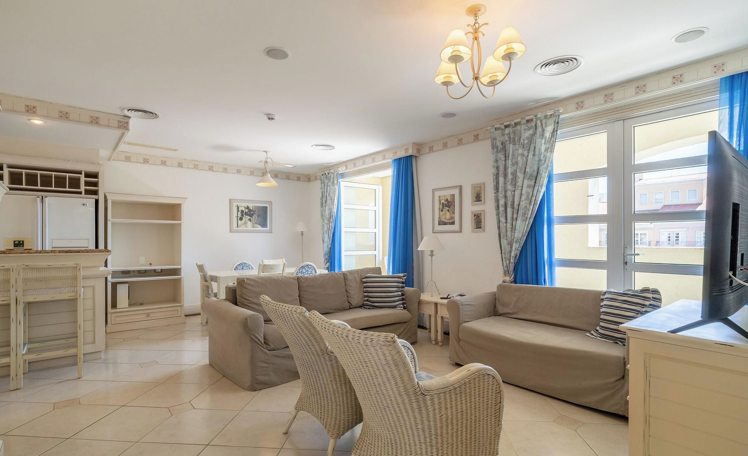 A living room with a sofa set, a wicker chair, a television, and a dining area with a table and chairs.