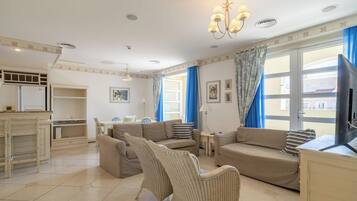 A living room with a sofa set, a wicker chair, a television, and a dining area with a table and chairs.