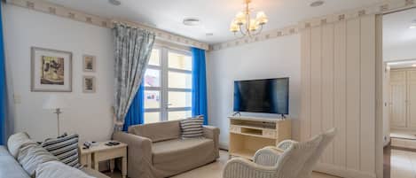 A living room with a sofa, armchair, TV, and a wicker chair.