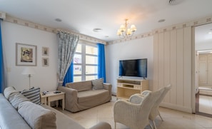 Een woonkamer met een bank, fauteuil, televisie en een rieten stoel.