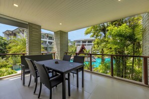 Un balcón con mesa y sillas, con vistas a una piscina y exuberante vegetación.