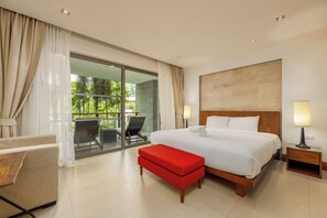 Ein Hotelzimmer mit einem großen Bett, einer roten Bank, einem Schreibtisch, einem Stuhl und einem Balkon mit Blick auf Grünflächen.