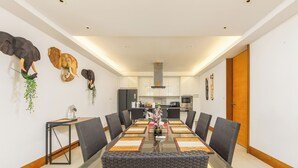 Comedor moderno con una mesa de vidrio, sillas tejidas negras y decoraciones de cabezas de elefante en la pared.