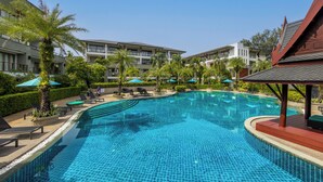 Una piscina con sillones de descanso y sombrillas, rodeada por un edificio con varios balcones.