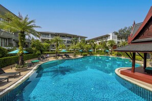 Ein Schwimmbecken mit Liegestühlen und Sonnenschirmen, umgeben von einem Gebäude mit mehreren Balkonen.