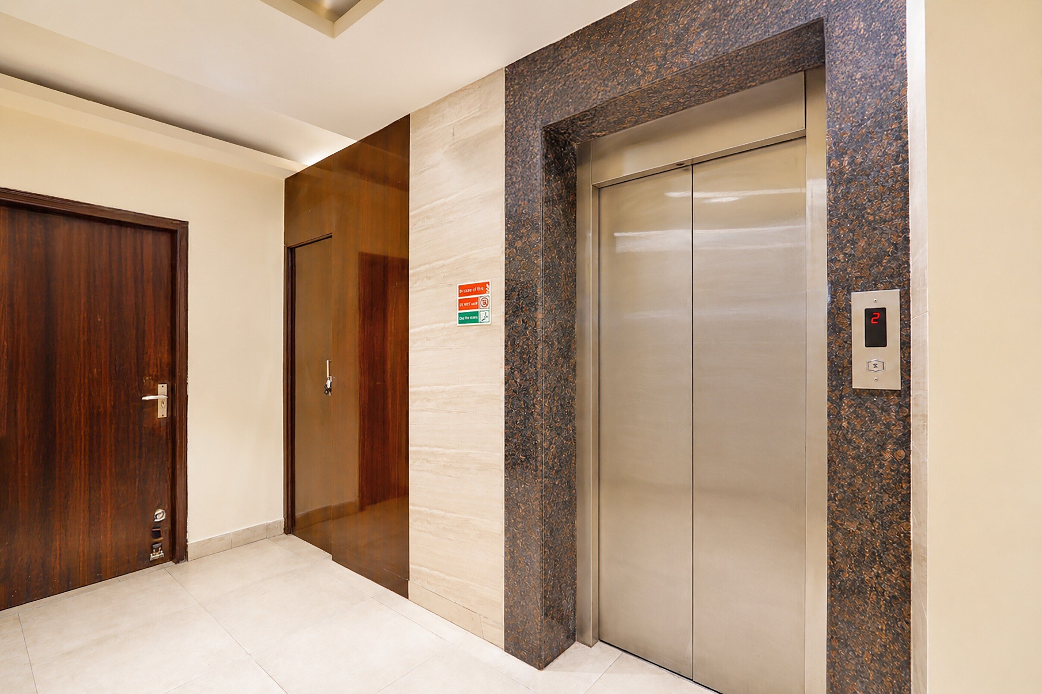 Un pasillo con puerta de madera, pared de mármol y un ascensor.
