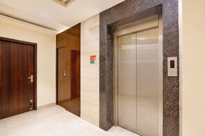 Un pasillo con puerta de madera, pared de mármol y un ascensor.