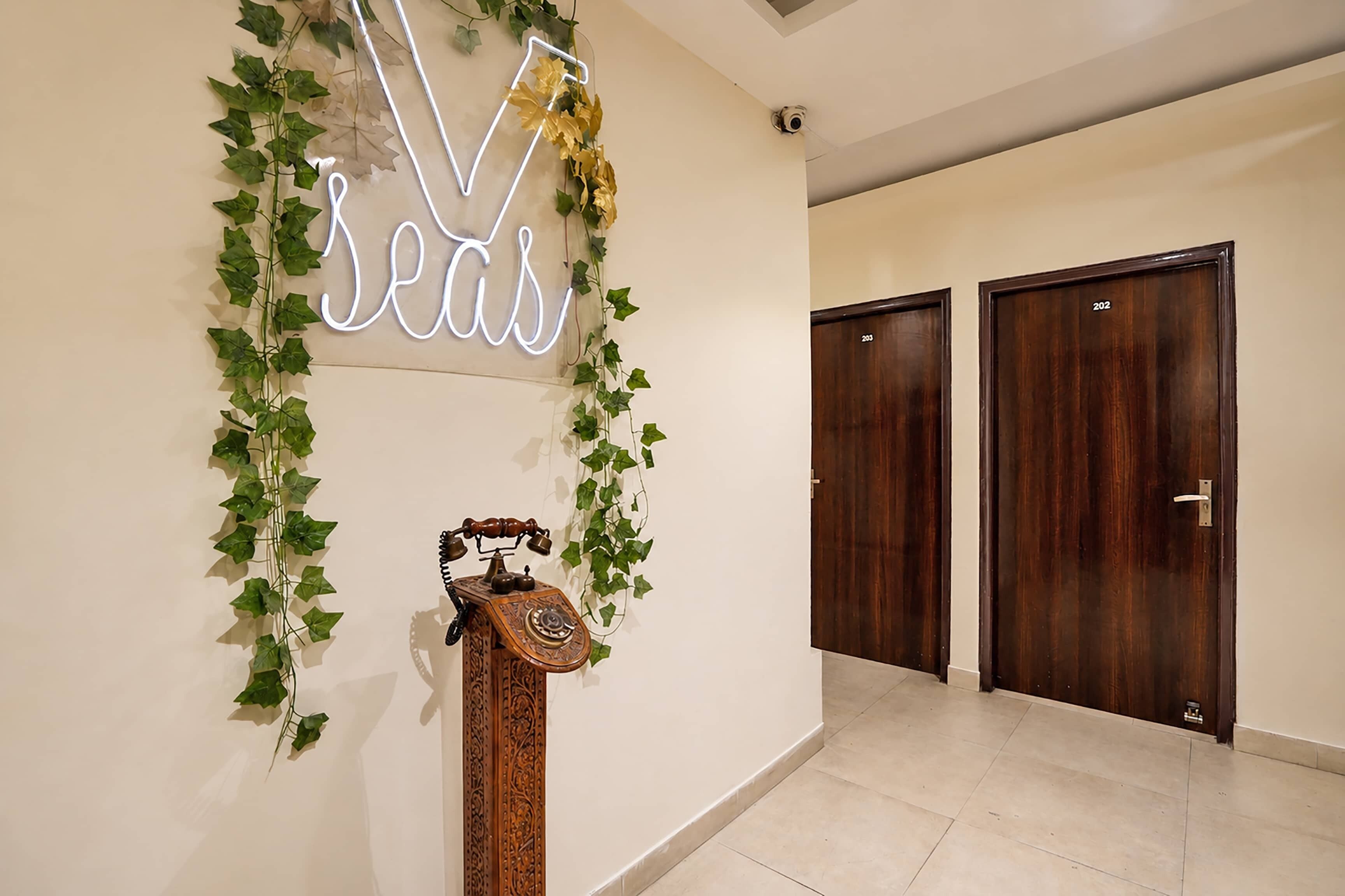 Un pasillo con un letrero de neón que dice 'seas', un teléfono de madera y dos puertas de madera.