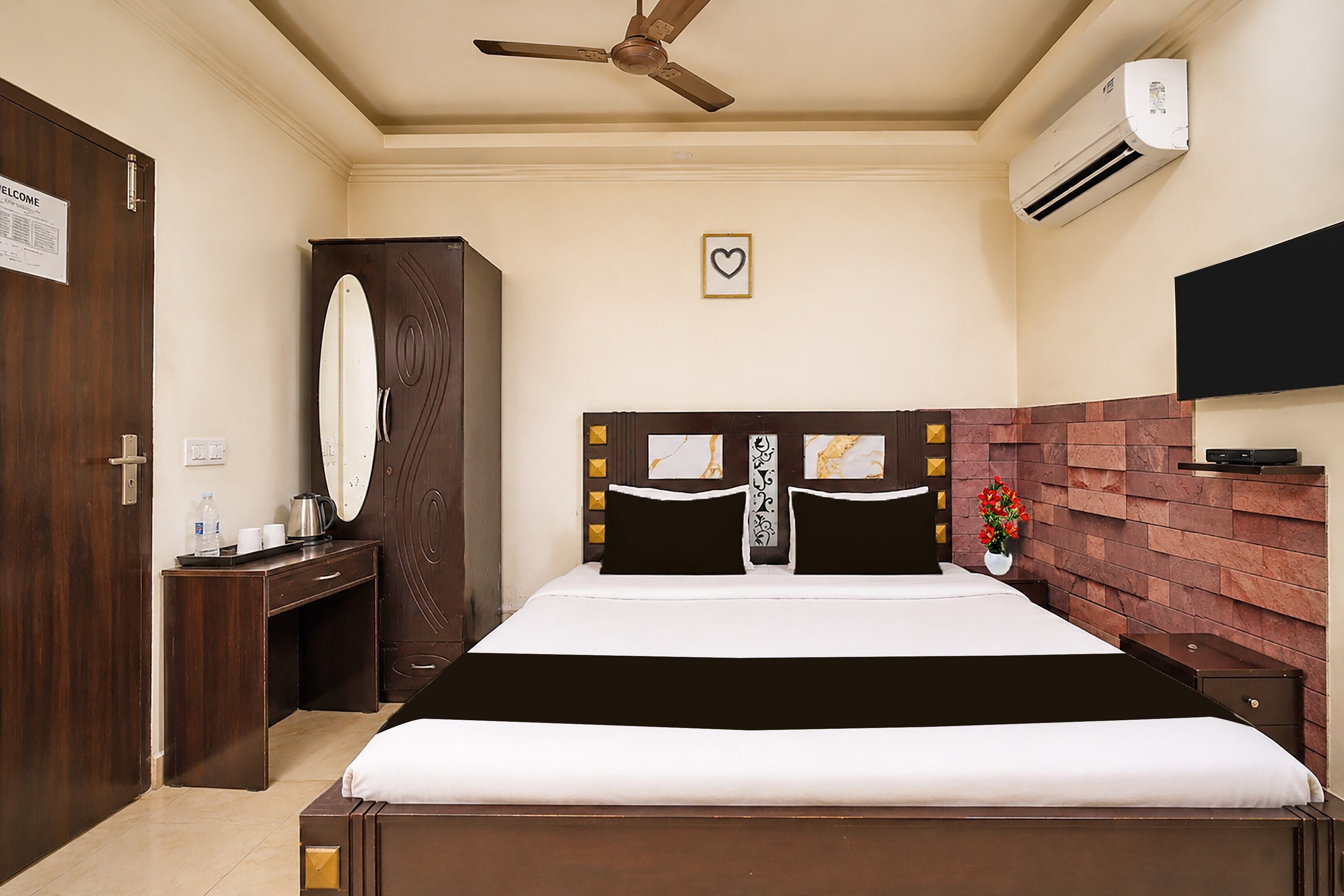 Ein Hotelzimmer mit Bett, Schreibtisch, Kleiderschrank, Deckenventilator, Klimaanlage und Fernseher.