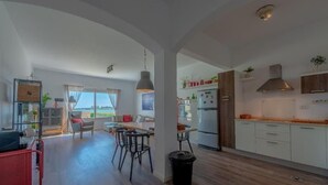 A modern kitchen with white cabinets, a stainless steel range hood, and a dining area with a table and chairs. - unique flat_ garden and lagoon (Hurghada)