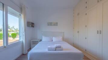 Un dormitorio con una cama grande, una mesita de noche, un armario y una ventana con cortinas.