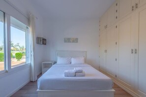 A bedroom with a large bed, a nightstand, a wardrobe, and a window with curtains.