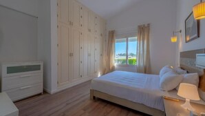 A bedroom with a bed, bedside table, lamp, wardrobe, and a view of greenery outside. - unique flat_ garden and lagoon (Hurghada)
