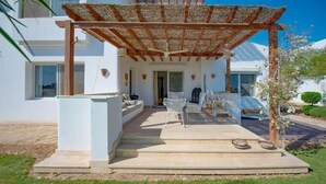 A covered outdoor seating area with a pergola, steps leading to a door, and a white building in the background. - unique flat_ garden and lagoon (Hurghada)