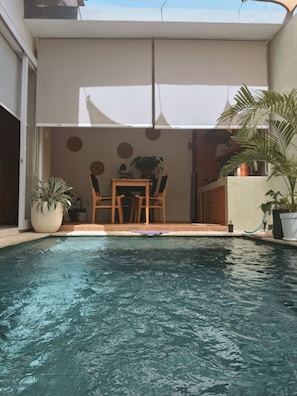 Ein Swimmingpool mit Tisch und Stühlen, umgeben von Topfpflanzen und einem Sonnenschirm.
