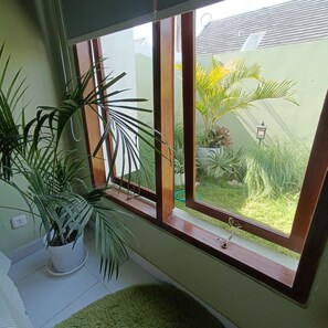 Ein Zimmer mit einem großen Fenster, einer Topfpflanze und einem kleinen Teppich.