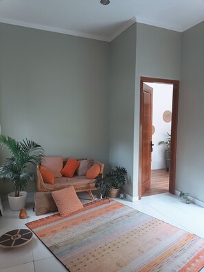 Une pièce comprenant un canapé, des plantes en pot, un tapis à motifs et une porte donnant sur une autre pièce.