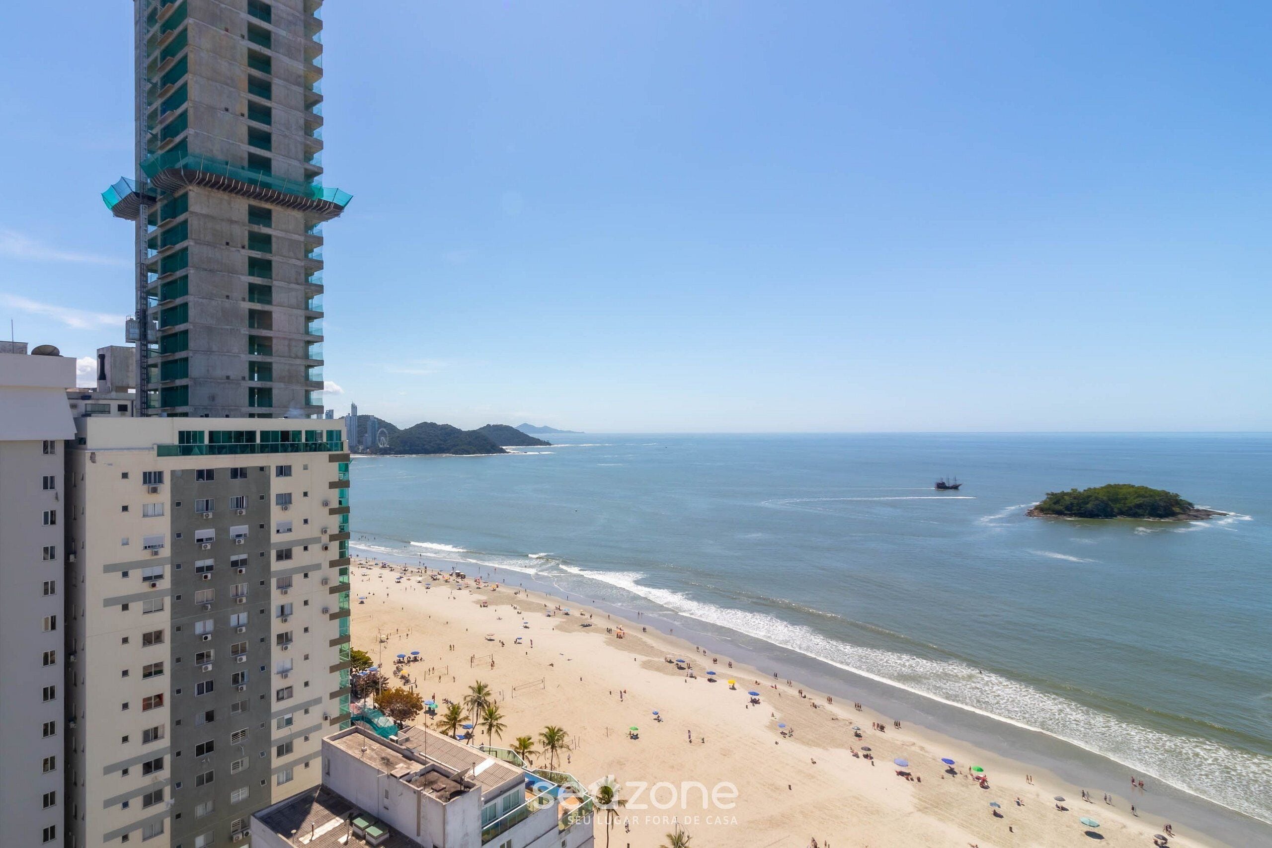 A beach with a high-rise building in the foreground and a small island in the distance.