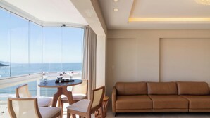 Ein modernes Hotelzimmer mit Balkon und Meerblick, einem runden Tisch mit zwei Stühlen sowie einem braunen Ledersofa.
