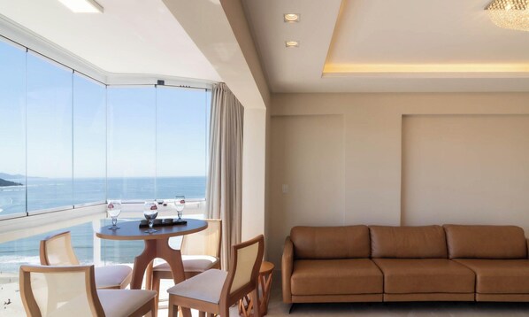 A modern hotel room with a balcony overlooking the sea, a round table with two chairs, and a brown leather sofa. - Apart w/ Side Sea View in Front of Beach Iptr0241 (Balneário Camboriú)