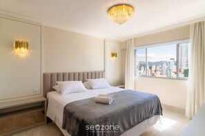 A modern hotel room with a large bed, city view, and elegant lighting fixtures. - Apart w/ Side Sea View in Front of Beach Iptr0241 (Balneário Camboriú)