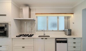 A kitchen with white cabinets, a built-in oven, a gas stove, a window with blinds, and a dishwasher. - Apart w/ Side Sea View in Front of Beach Iptr0241 (Balneário Camboriú)