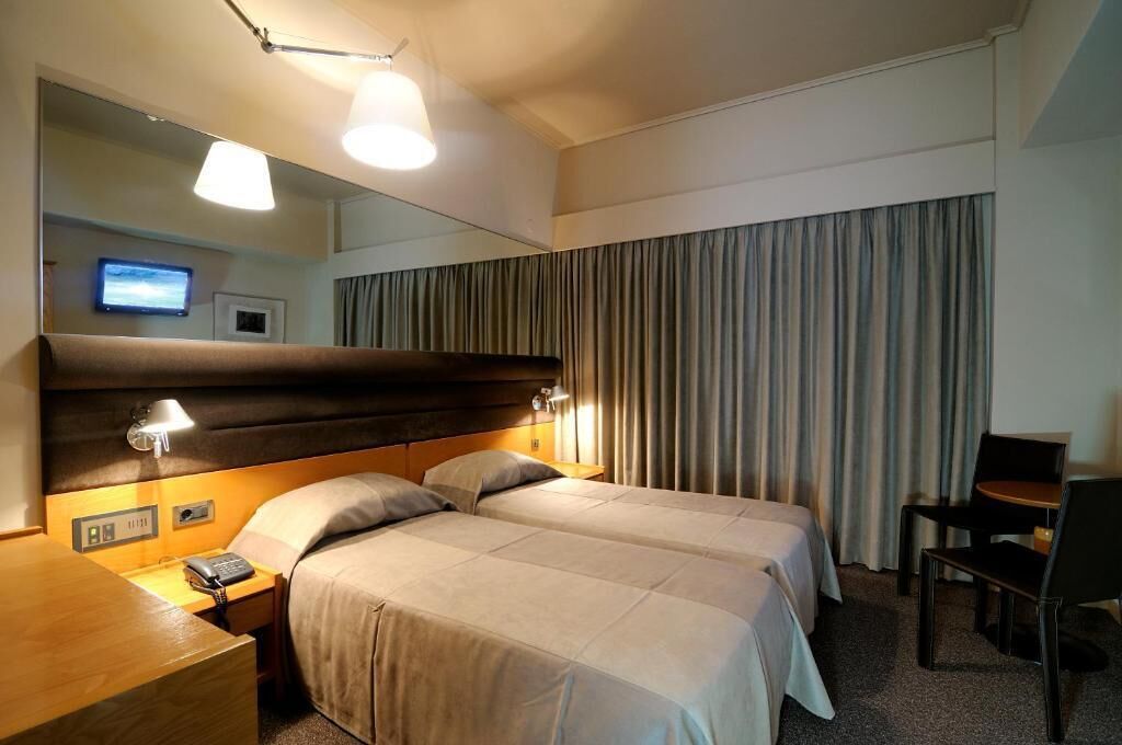 A hotel room with two beds, a desk with a telephone, a chair, a mirror, and a television on the wall.