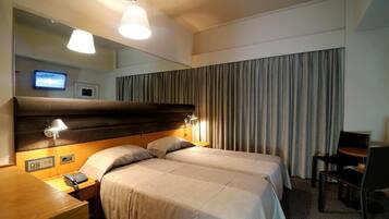 A hotel room with two beds, a desk with a telephone, a chair, a mirror, and a television on the wall.