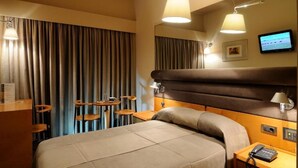 Una habitación de hotel con cama, mesita de noche, lámpara y televisión instalada en la pared.