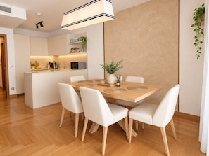 A modern kitchen with white cabinets, a wooden dining table with white chairs, and a hanging plant. - Mare Blu - Portopiccolo Apartments (Sistiana)