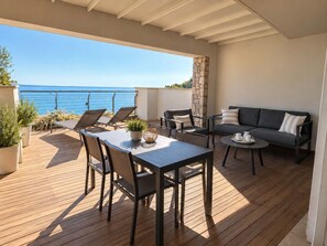 A wooden deck with a table and chairs, a sofa, and a stone pillar. - Mare Blu - Portopiccolo Apartments (Sistiana)