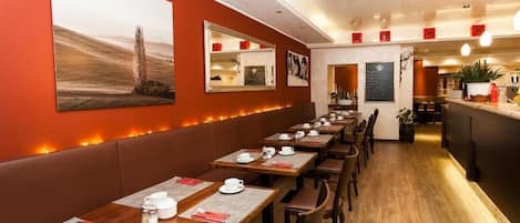 Un restaurante con largas mesas de madera, asientos tapizados y un ambiente cálido con luces en la pared.