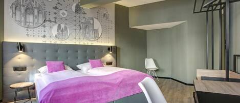 A modern bedroom with a large bed, a headboard, a wall art piece, and a desk area.