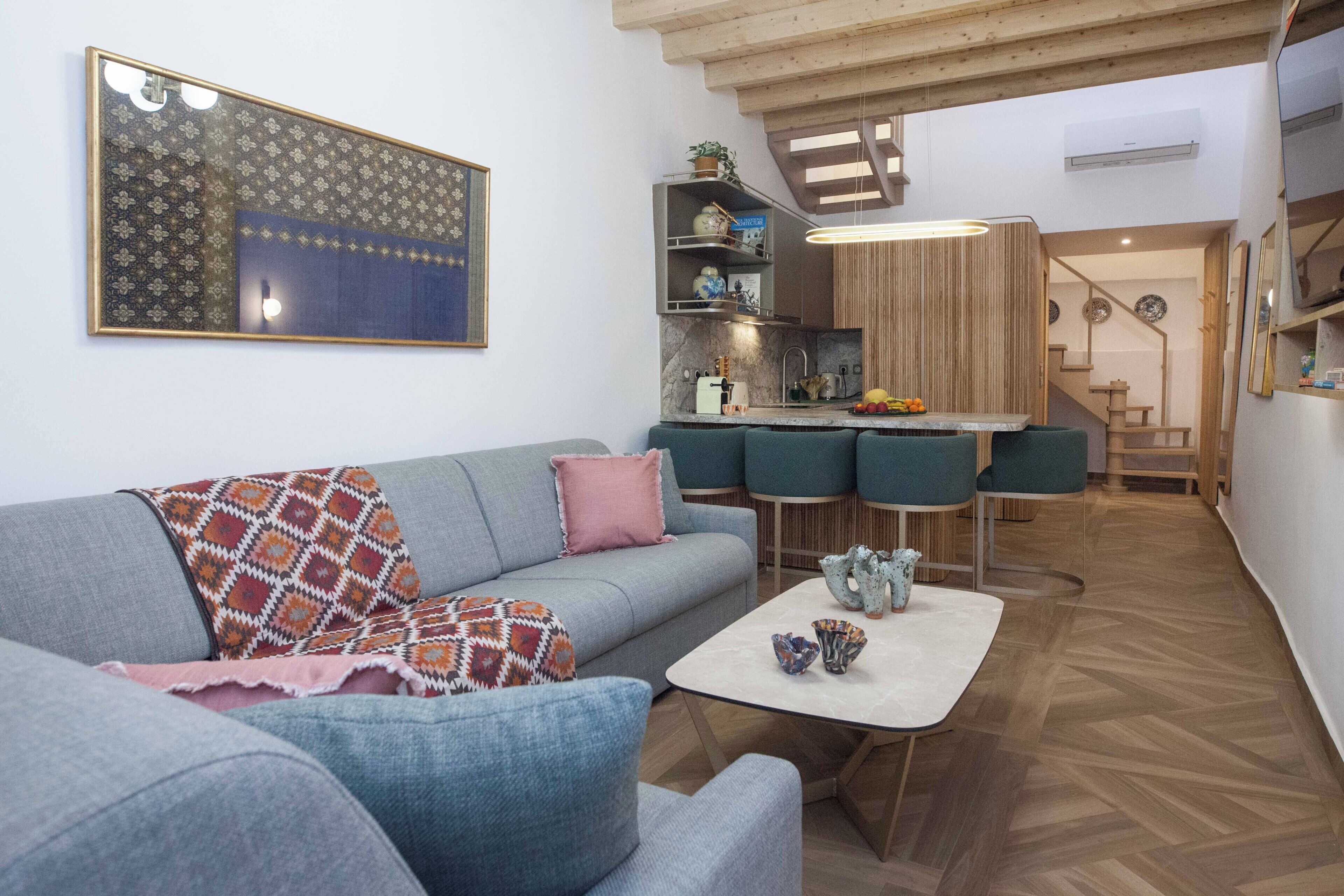 Un salon moderne avec un canapé gris, une table basse et un coin cuisine équipé de tabourets de bar.