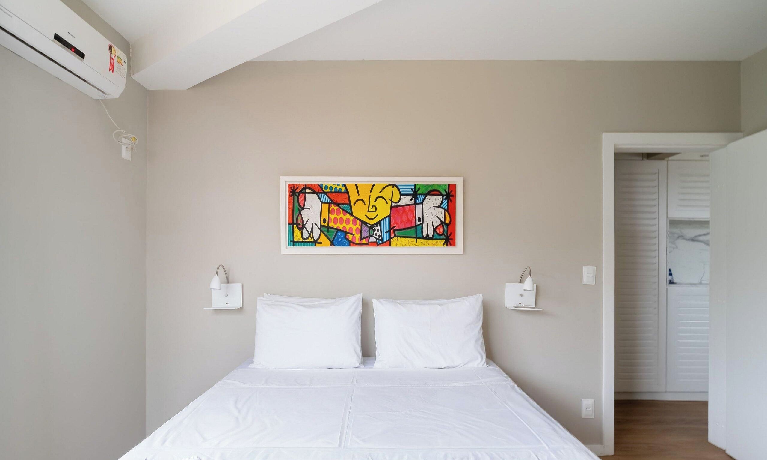 Une chambre à coucher avec un lit, un tableau abstrait aux couleurs vives et un appareil de climatisation blanc.