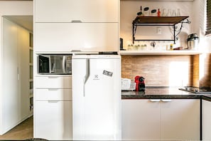 Cozinha compacta com geladeira, micro-ondas e uma cafeteira vermelha no balcão.