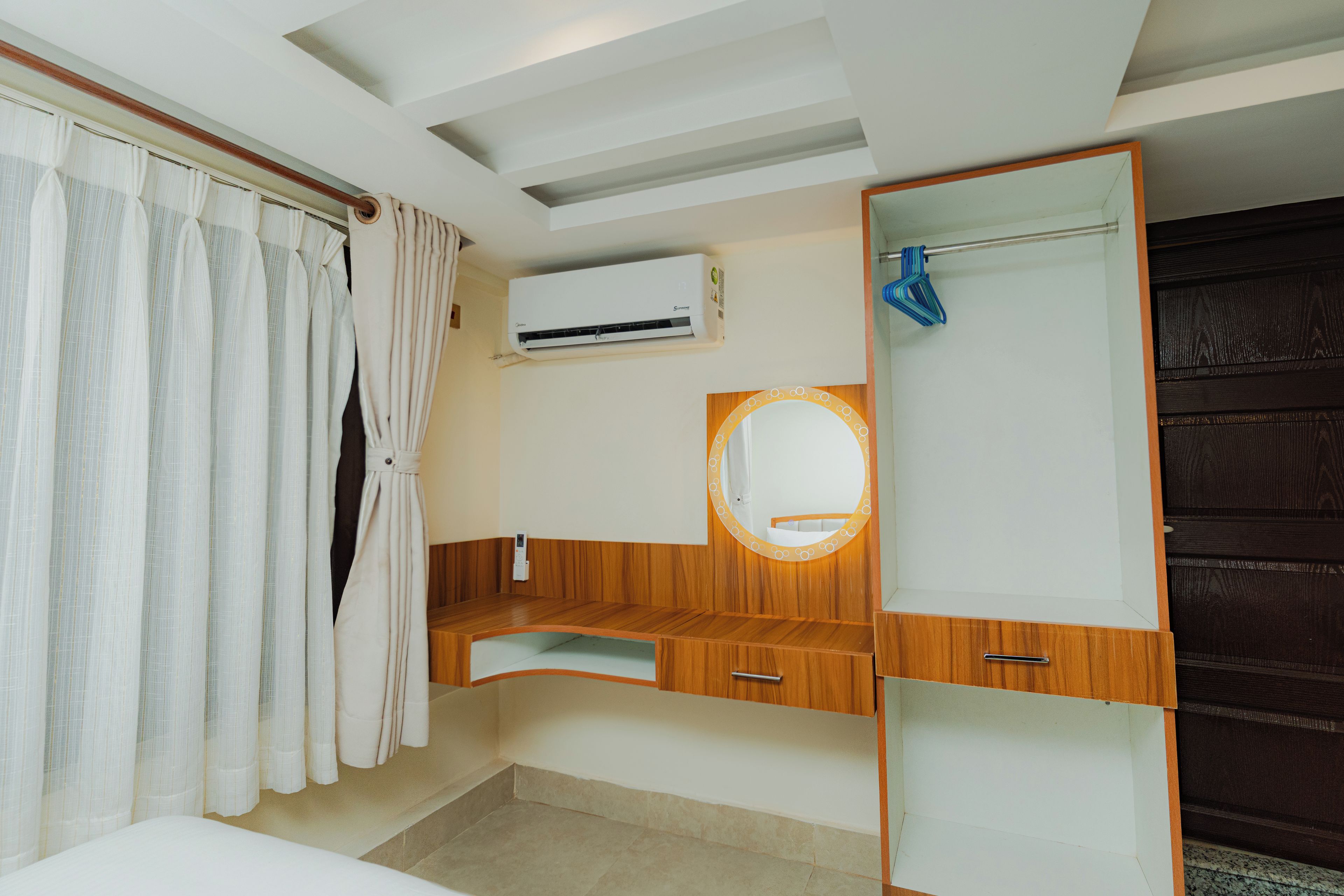 Een slaapkamer met een bed, een kaptafel met spiegel, een airconditioning en een raam met gordijnen.