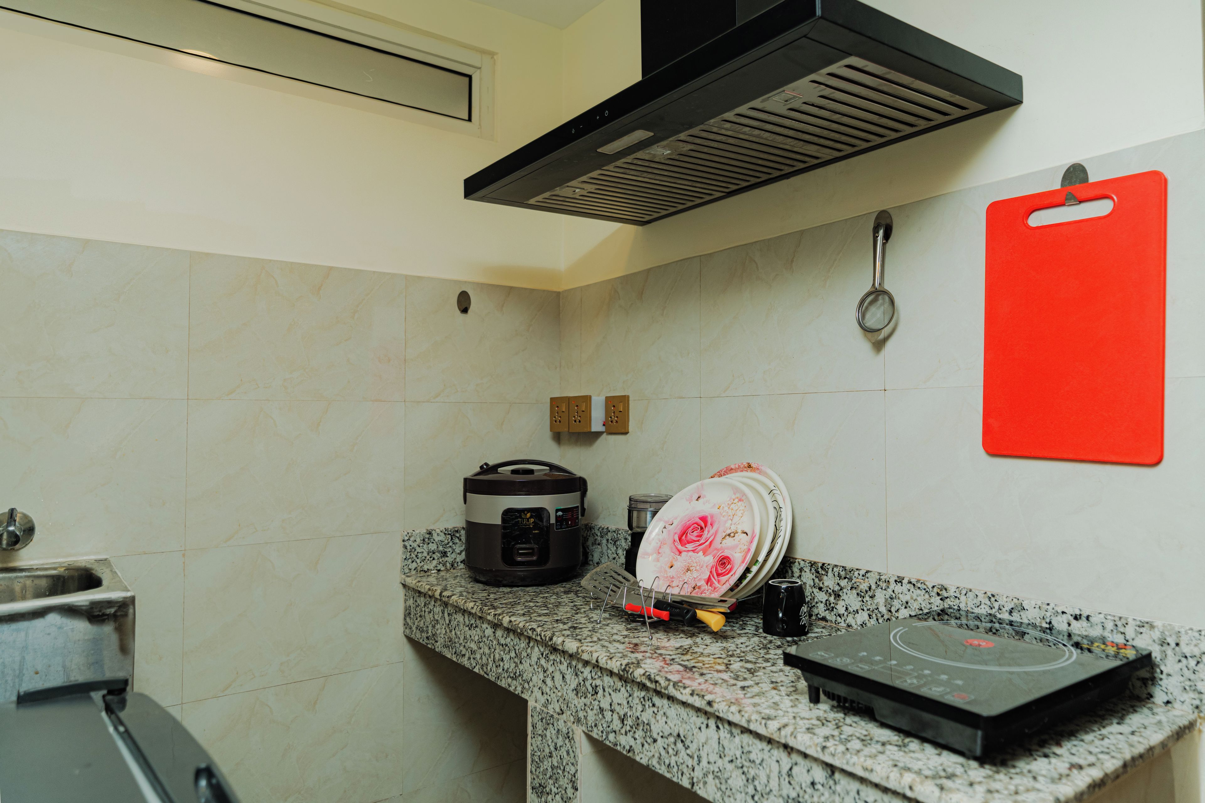 A kitchen with a built-in oven, a rice cooker, a dish rack, and a red cutting board.
