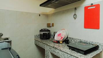A kitchen with a built-in oven, a rice cooker, a dish rack, and a red cutting board.